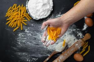 mano Tenere pasta su nero sfondo prima cucinando. preparazione pasta. Farina su un' sfondo. foto