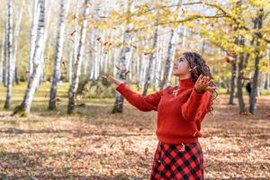 giovane donna felice che getta foglie nella foresta autunnale foto