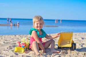 contento bambino piccolo bambino giocando su il spiaggia con giocattolo macchina, ragazza guardare per il camera.family estate vacanza viaggio concetto. copia spazio. foto