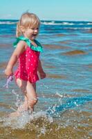 giovane contento bambino ragazza di europeo aspetto età di 4 avendo divertimento nel acqua su il spiaggia e spruzzi,tropicale estate vocazioni,vacanze.a bambino gode il mare.verticale fotocopia spazio foto