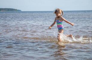 giovane contento bambino ragazza di europeo aspetto età di 6 avendo divertimento nel acqua su il spiaggia e spruzzi,tropicale estate vocazioni,vacanze.a bambino gode il mare.famiglia vacanze concetto.copia spazio. foto