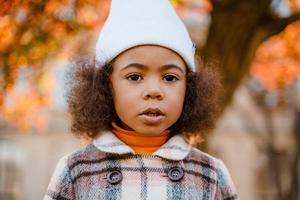 ragazza riccia nera che indossa un cappello bianco che cammina nel parco autunnale foto