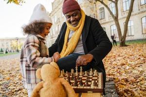 nonno nero e nipote che giocano a scacchi nel parco autunnale foto