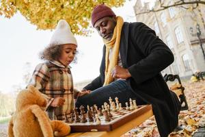 nonno nero e nipote che giocano a scacchi nel parco autunnale foto