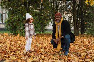 nonno nero e nipote che si divertono con le foglie cadute nel parco autunnale