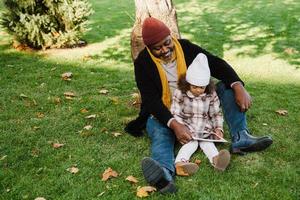 nonno e nipote neri che utilizzano il computer tablet mentre sono seduti nel parco foto