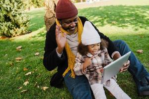 nonno e nipote neri che utilizzano il computer tablet mentre sono seduti nel parco foto