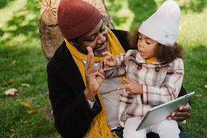 nonno e nipote neri che utilizzano il computer tablet mentre sono seduti nel parco foto