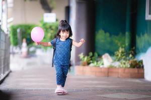 adorabile bambina tiene in mano un palloncino rosa che corre su un pendio. lei tese le braccia. indossare abiti blu scuro. lei sorrise dolcemente. bambini dai due agli otto mesi. indossare scarpe rosa con pelliccia morbida. foto