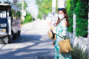 donna adolescente che indossa una maschera a forma di 4d. bella persona viaggia in un modo nuovo e normale. viaggiare in vacanza durante la diffusione dell'epidemia di coronavirus covid19. cappelli di paglia e borse in tessuto. macchina sulla strada foto