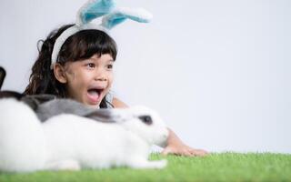 sorridente poco ragazza e con loro Amati soffice coniglio, in mostra il bellezza di amicizia fra gli esseri umani e animali foto