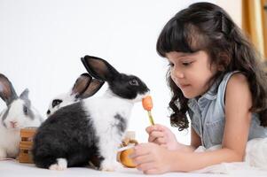 sorridente poco ragazza e con loro Amati soffice coniglio, in mostra il bellezza di amicizia fra gli esseri umani e animali foto