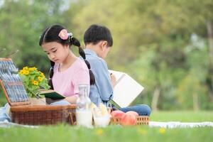 contento famiglia godendo un' picnic nel il parco, bambini seduta indietro per indietro e lettura libri. foto