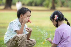 bambini seduta nel il parco con soffiaggio aria bolla, circondato di verdura e natura foto