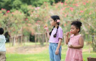 bambini seduta nel il parco con soffiaggio aria bolla, circondato di verdura e natura foto