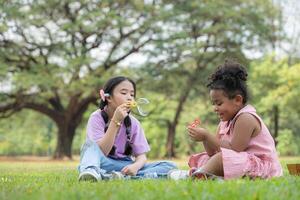 bambini seduta nel il parco con soffiaggio aria bolla, circondato di verdura e natura foto