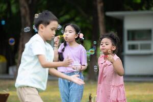 bambini seduta nel il parco con soffiaggio aria bolla, circondato di verdura e natura foto