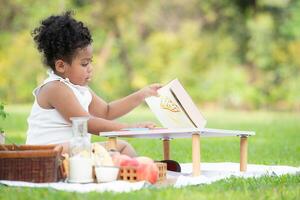 contento famiglia godendo un' picnic nel il parco, ragazza siamo avendo divertimento disegno su carta posto su il tavolo. foto