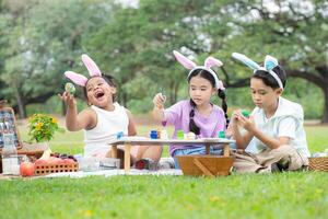 contento famiglia godendo un' picnic nel il parco, bambini seduta e colorazione loro bellissimo Pasqua uova. foto