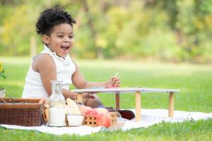 contento famiglia godendo un' picnic nel il parco, ragazza siamo avendo divertimento disegno su carta posto su il tavolo. foto