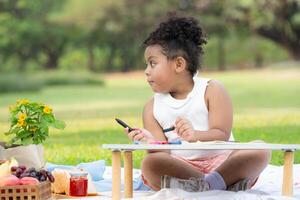 contento famiglia godendo un' picnic nel il parco, ragazza siamo avendo divertimento disegno su carta posto su il tavolo. foto