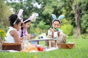 contento famiglia godendo un' picnic nel il parco, bambini seduta e colorazione loro bellissimo Pasqua uova. foto