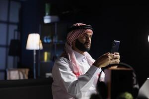 mezzo orientale imprenditore lavori diligentemente a il suo ufficio scrivania, utilizzando un' smartphone per in linea comunicazione e ricerca. Immagine Spettacoli arabo uomo a il tavolo Tenere un' digitale mobile dispositivo. foto