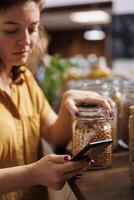 vegano donna su un' dieta utilizzando Telefono per rendere sicuro zero rifiuto supermercato cibo è bene per sua Salute. cliente nel Locale Quartiere drogheria memorizzare fabbricazione sicuro prodotti siamo naturale foto