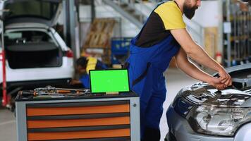 panning tiro di verde schermo il computer portatile nel box auto spazio di lavoro, seduta su opera panchina Il prossimo per professionale utensili con meccanica nel sfondo Lavorando su macchine, utilizzando coppia chiave inglese per fix loro foto