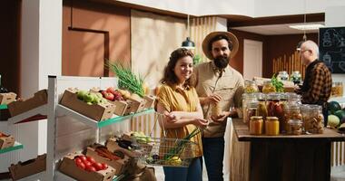 Ingrandisci su tiro di contento verde vivente coppia acquisto dispensa graffette a partire dal zero rifiuto supermercato. sorridente i clienti shopping per massa cibo prodotti nel riutilizzabile barattoli a partire dal Locale Quartiere memorizzare foto