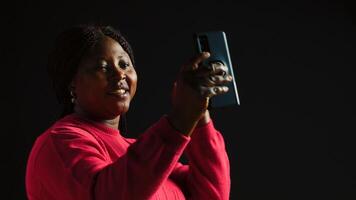 un' allegro donna nel nero sfondo agitando a un' video chiamata su sua smartphone avendo un' lontano interazione su un Internet video conferenza. discussione su mobile Telefono attraverso video conferenza. foto