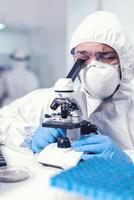 vicino su di medico ingegnere fare ricerca su covid virus indossare pp. scienziato nel protettivo completo da uomo seduta a posto di lavoro utilizzando moderno medico tecnologia durante globale epidemico. foto