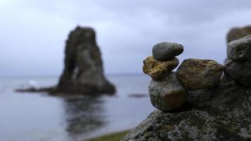 avvicinamento di impilati rocce su spiaggia con rocce. clip. pietre impilati nel composizione su sfocato sfondo di rocce nel mare. pietre impilati nel torretta In piedi su sfondo di nuvoloso mare foto