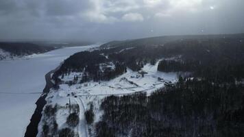 aereo Visualizza di panoramico natura nel inverno stagione con piccolo villaggio e fiume. clip. volante neve e il inverno freddo sole splendente su pino albero foresta. foto