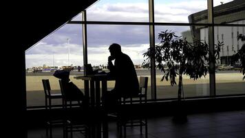 uomo d'affari in attesa per imbarco a il aeroporto e guardare attraverso panoramico finestre. silhouette di un' uomo a un' tavolo con ombre di passaggio le persone. foto