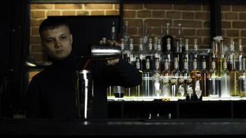 il barista preparazione Perfetto cocktail, in piedi dietro a il bar contatore. media. molti bottiglie di alcool su il sfondo. foto