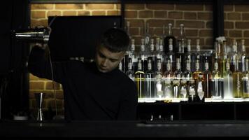 il barista preparazione Perfetto cocktail, in piedi dietro a il bar contatore. media. molti bottiglie di alcool su il sfondo. foto