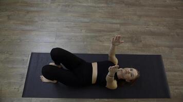 mattina yoga allenarsi a casa. media. giovane sottile donna esercizio e dire bugie su stuoia, raccolta sua braccia e gambe. foto