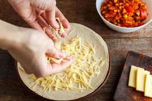 una donna spruzza una torta di formaggio per la tortilla di quesadilla. produzione di quesadilla in casa. foto