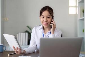 giovane asiatico attività commerciale donna parlare su smartphone Scrivi taccuino il computer portatile nel ufficio. avviare attività commerciale donna in linea pmi telemarketing foto