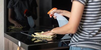 asiatico donna pulizia il tavolo superficie con asciugamano e spray detergente foto