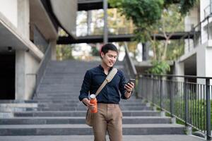 sorridente asiatico uomo d'affari a piedi per opera mentre per hold riutilizzabile eco amichevole ecologico tazza nel il città foto