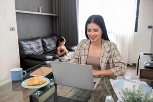 attività commerciale donna o mamma Lavorando con sua poco figlia a un' il computer portatile. libero professionista, opera a partire dal casa foto