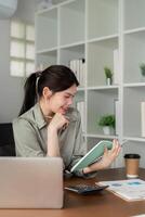 asiatico attività commerciale donna utilizzando il computer portatile per analisi grafico finanziario bilancio rapporto e pianificazione per futuro nel ufficio scrivania foto