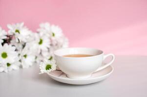bianca impostato tazza con un' piatto per tè e caffè In piedi su un' rosa sfondo con camomilla fiori foto