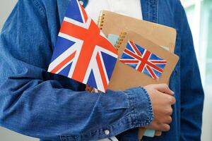 apprendimento inglese, asiatico adolescenziale alunno Tenere libro con bandiera per linguaggio programma formazione scolastica. foto