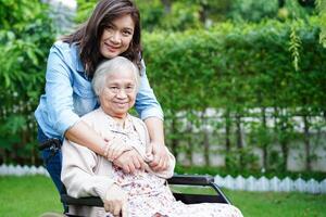 il caregiver aiuta il paziente con disabilità della donna anziana asiatica seduto su una sedia a rotelle nel parco, concetto medico. foto
