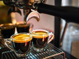 vicino su di caffè espresso tiro con caffè crema e professionale caffè macchina mentre preparazione Due espresso tiro bicchiere nel un' caffè negozio. foto