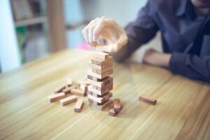 attività commerciale strategia concetto con mani giocando un' di legno bloccare Torre gioco, simboleggiante rischio e stabilità. pianificazione rischio gestione foto