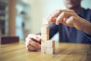 mano strategicamente collocazione di legno blocchi nel un' scalino design su un' tavolo, significare progressivo successo e crescita foto